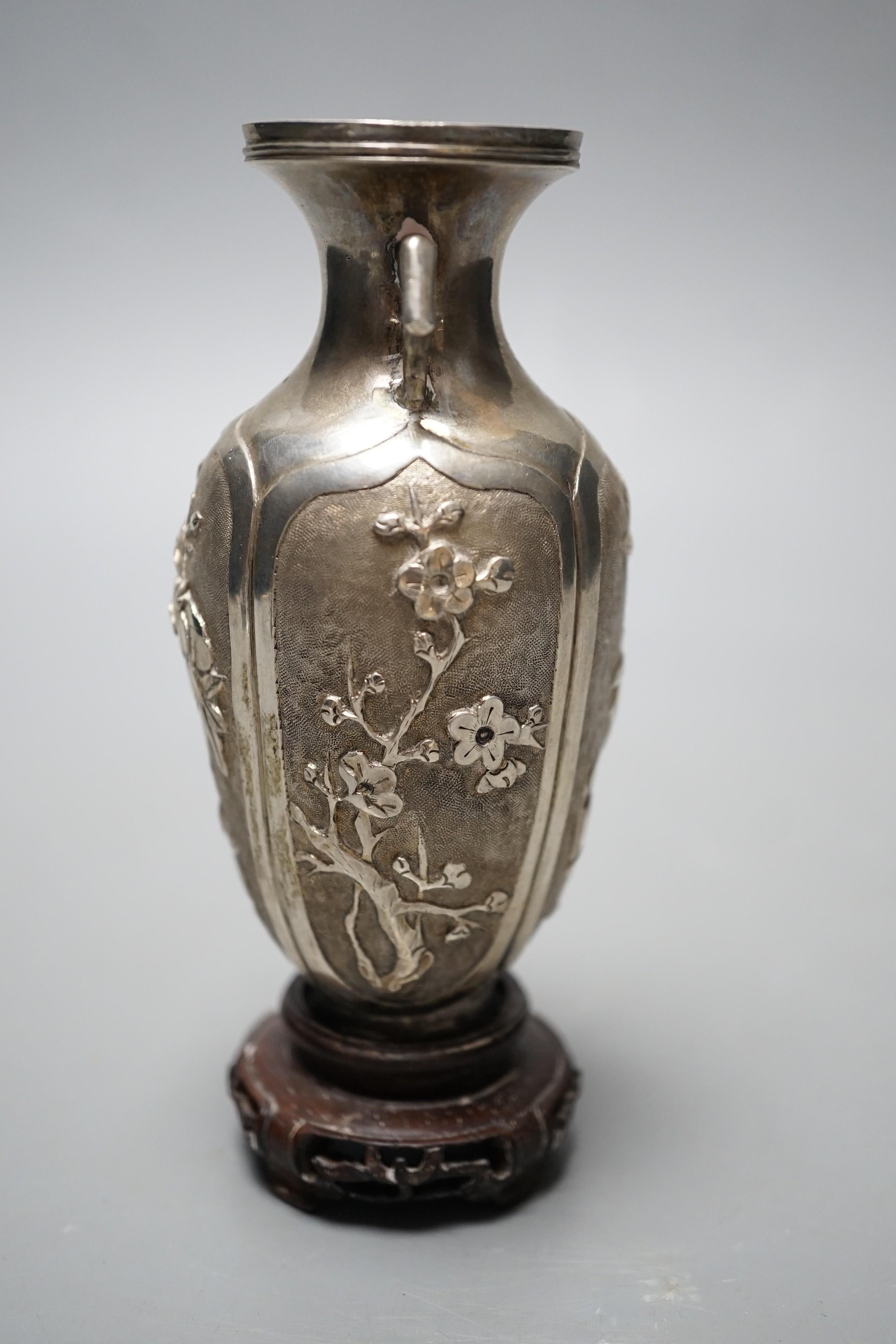 A late 19th/early 20th century Chinese Export white metal two handled vase, decorated with bamboo, peonies and prunus, on hardwood stand with white metal wing nut signed Zee Wo, vase 12cm.
